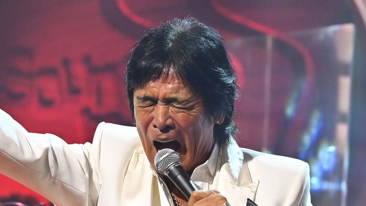 手を上げながらマイクで歌う松崎しげる