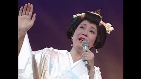 白い衣装でマイクを持つ島倉千代子（コロムビアのコンサート紹介写真、撮影年・曲は不明）