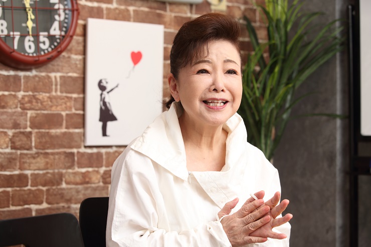 白いブラウス姿で両手を組み、取材に臨む中村美律子